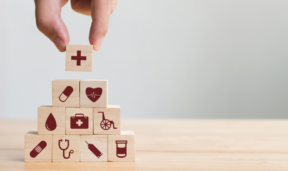 A stack of wooden blocks each containing a different healthcare symbol. Among the symbols are the cross, a heartbeat, a stethoscope, and band-aids.